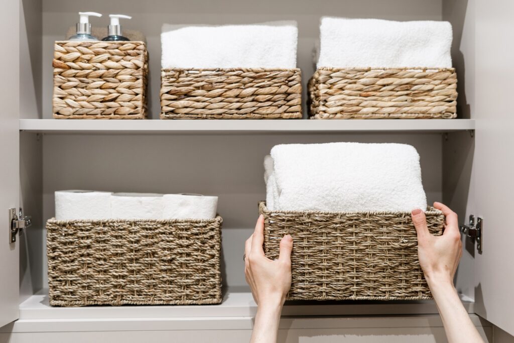 Cropped view of housewife putting box with clean bath towels on shelf in closet with household items. Neatly room and concepts of organization of tidy space in the bathroom cabinet
